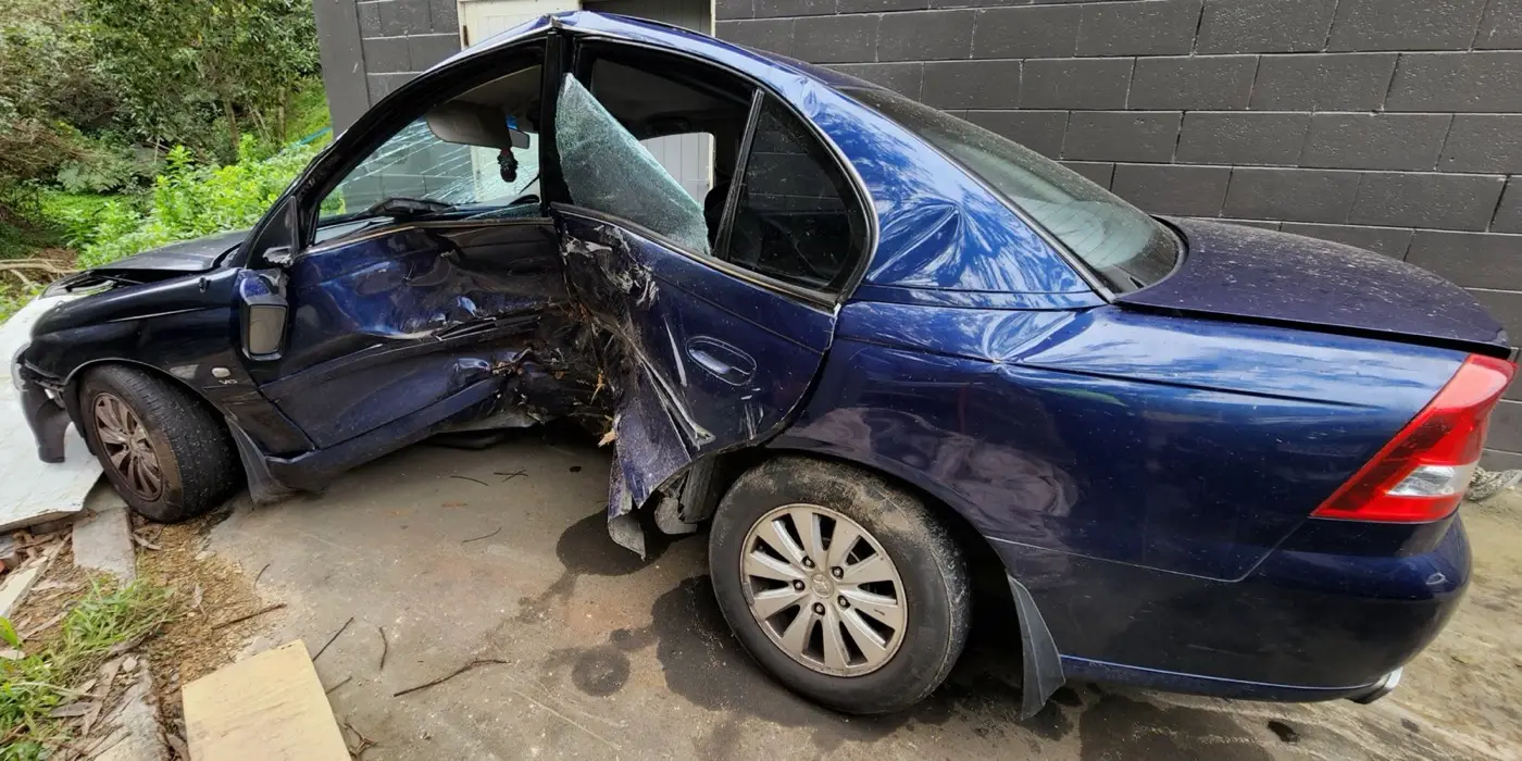A blue car with heavy impact damage to its left side.
