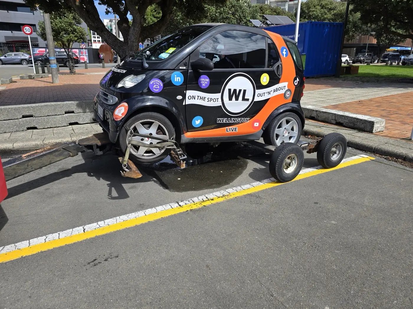 A vehicle with its front wheels raised by a tow truck and its rear wheels raised onto a towing dolly.