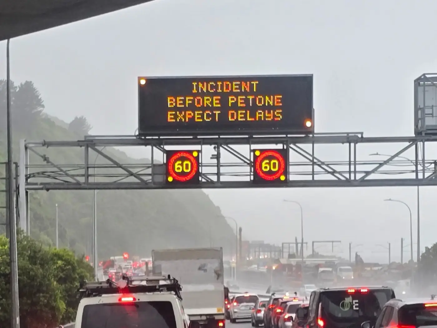 A motorway sign says INCIDENT BEFORE PETONE EXPECT DELAYS above a long line of traffic.