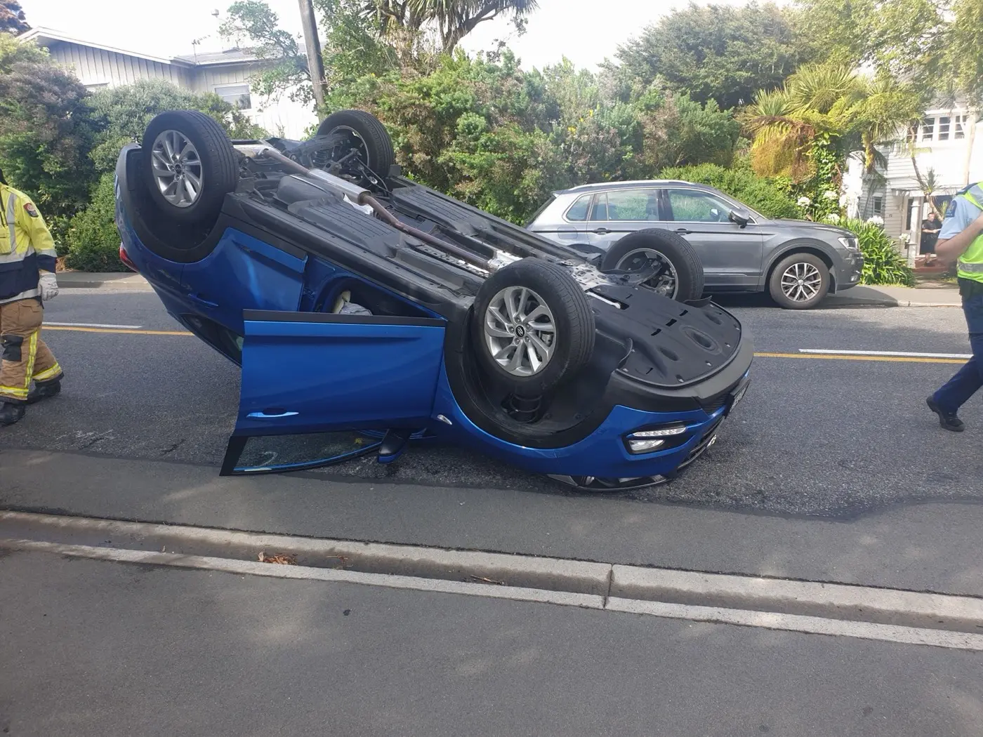 A blue vehicle overturned in the roadway with a door open.