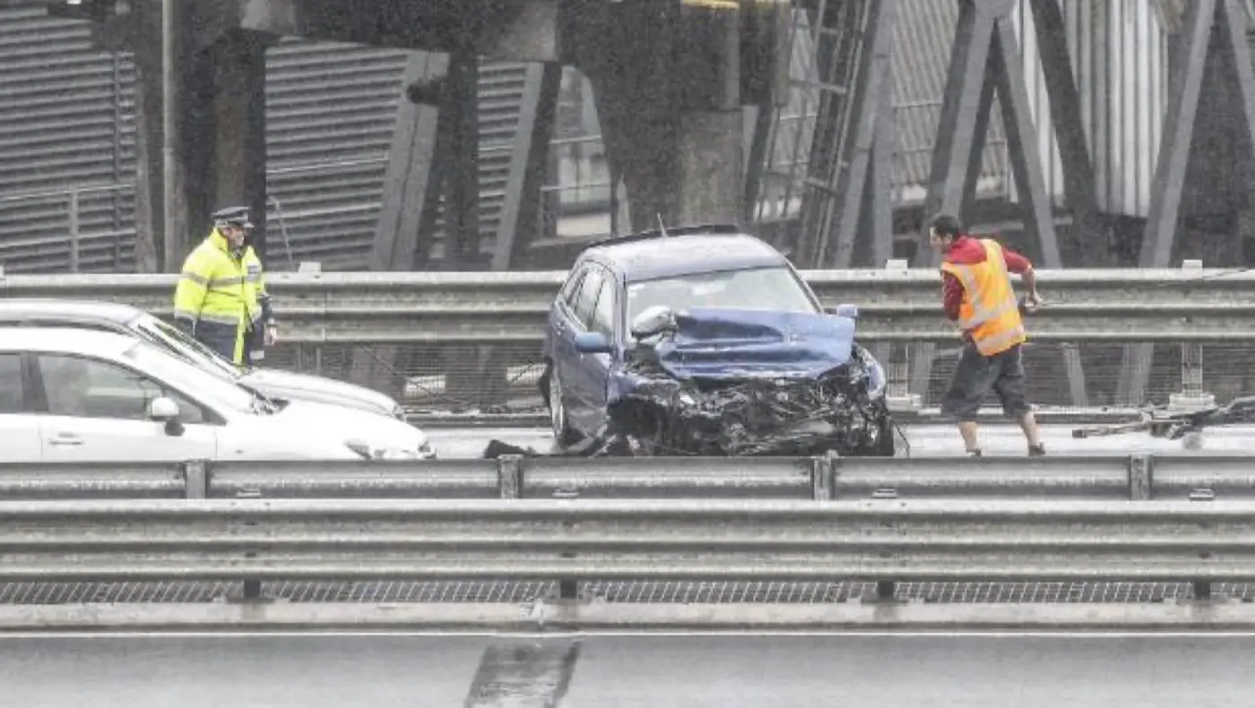 A police officer watches a Jamieson's driver on the Wellington Urban Motorway attaching a winch line to a car with major front damage.