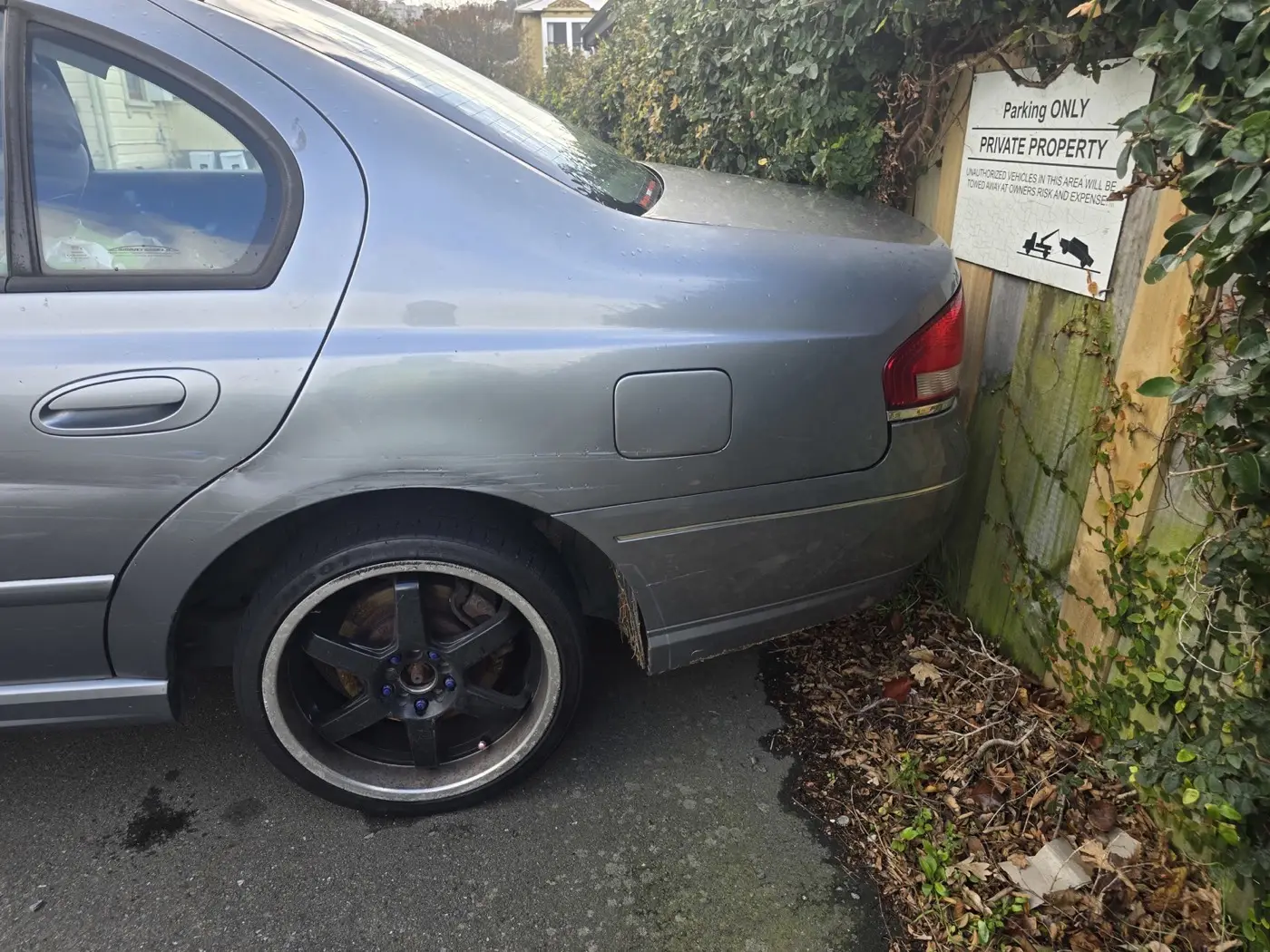 The rear of a car parked in front of a sign saying the area is private property and vehicles will be towed.