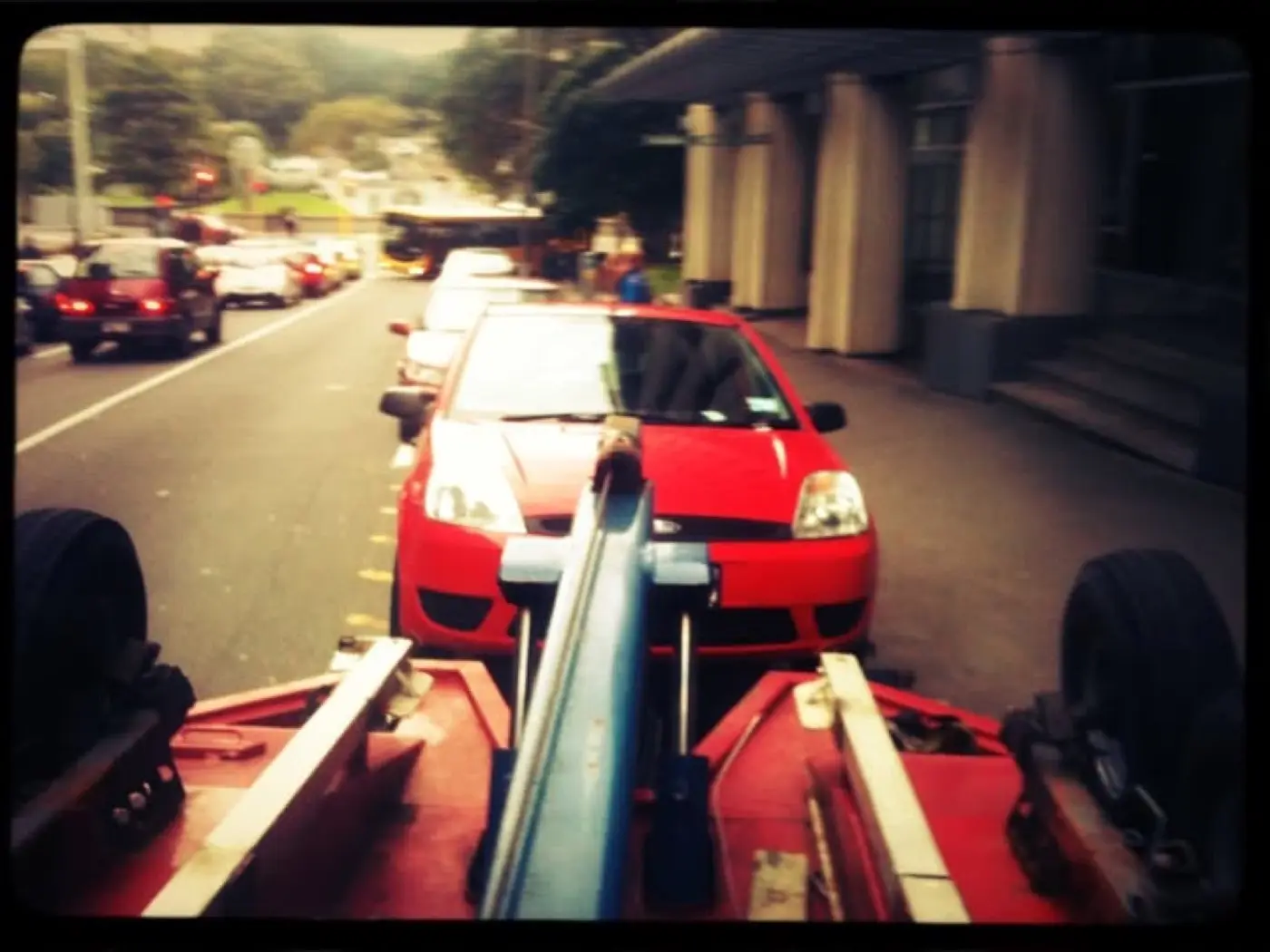A red car lifted by a Jamieson's tow truck, seen from the cab of the truck.