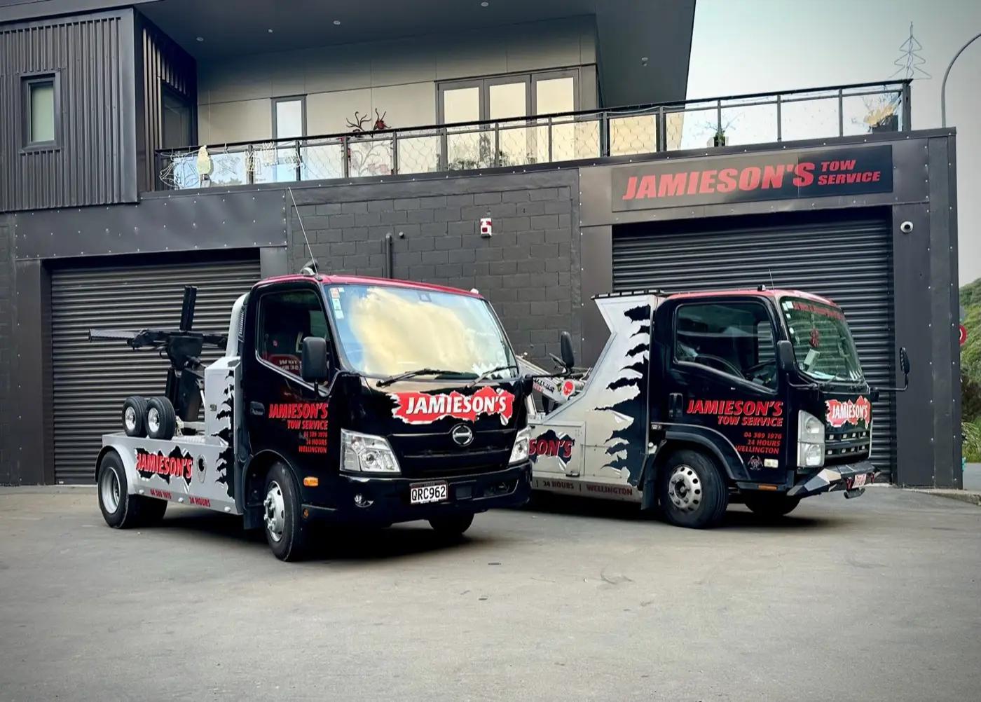 Two Jamieson's tow trucks parked beneath a sign that says Jamieson's Tow Service, at 509 Ohiro Road.