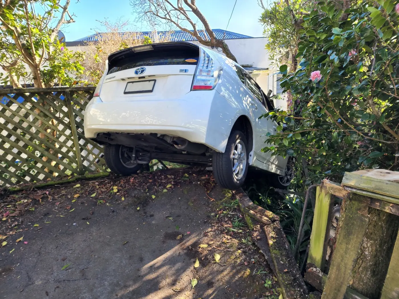 A white car that has come off the road and come to rest with its rear wheels in the air.